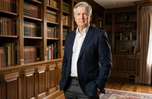 Homme élégant aux cheveux argentés portant un blazer marine taillé sur mesure dans une bibliothèque en bois sombre, style vestimentaire masculin après 60 ans